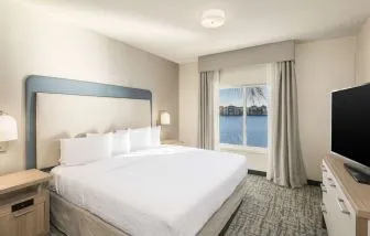 King bed with TV and a view of the Blue Lagoon at Homewood Suites By Hilton Miami Airport-Blue Lagoon.