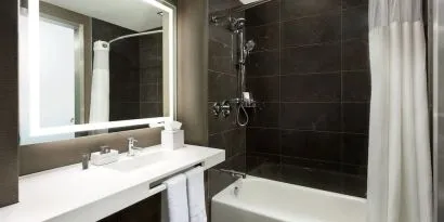 Private guest bathroom with combined shower and tub at AC Hotel New York Times Square.