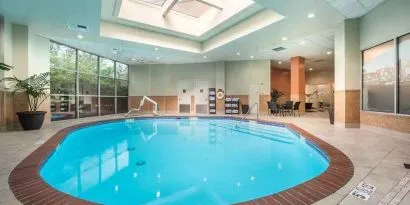 Bright-lit indoor pool with sun roof and comfortable seating area at Embassy Suites by Hilton Seattle Tacoma International Airport.