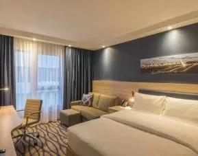 Queen room with sofa and desk at the Hampton by Hilton Frankfurt Airport.