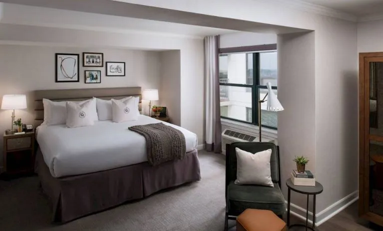 Double bed guest room in Claridge House, with art on the wall, window, and comfortable chair, footstool, and coffee table.