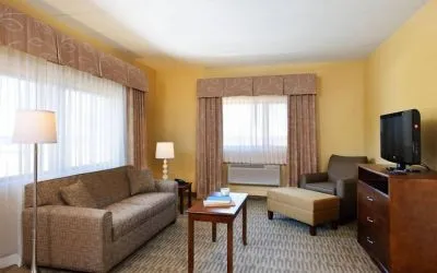 Guest room lounge in Holiday Inn Express Philadelphia Airport, with sofa, chair, TV, and foot stool.