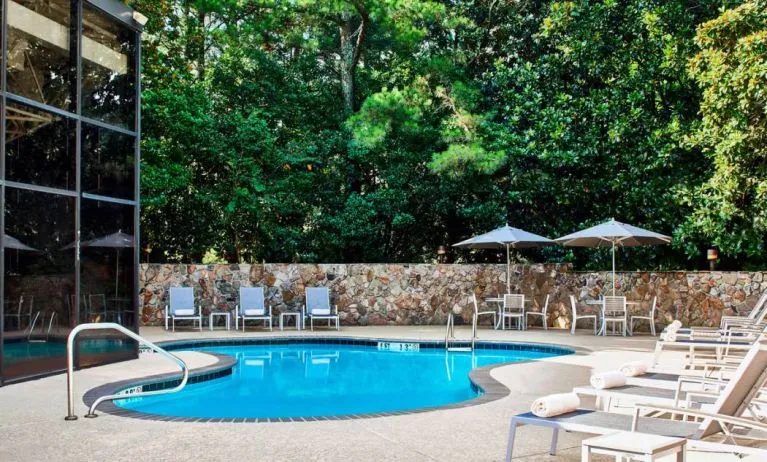 The hotel’s outdoor swimming pool has surrounding loungers and nearby trees.