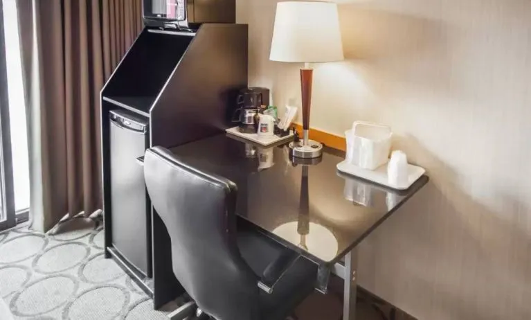 Closer shot of an in-room workspace, including chair, desk, lamp, and nearby window.
