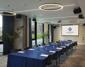 Meeting room with space for over a dozen attendees, featuring large windows and potted plants.