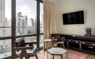 Guest room in The Draper, Ascend Hotel Collection, with two chairs, coffee table, large television, and urban vista through the window.
