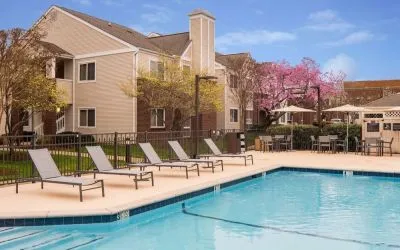 Shaded tables and chairs, as well as sun loungers, are by the side of Sonesta ES Suites Nashville Brentwood’s outdoor pool.