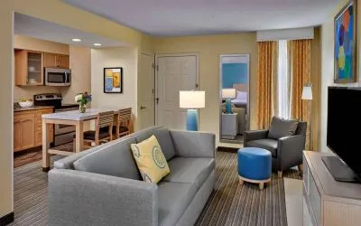 Sonesta ES Suites Cincinnati - Blue Ash guest room lounge, with armchair, sofa, and television, plus nearby kitchenette.