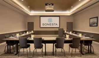 Hotel meeting room with long tables arranged in a U-shape, facing a large projector screen.