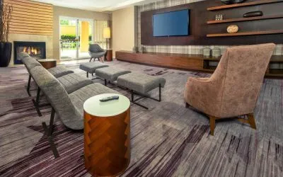 The hotel lobby is furnished with a very large TV, comfortable seating with footstools, a fireplace, and coffee tables.