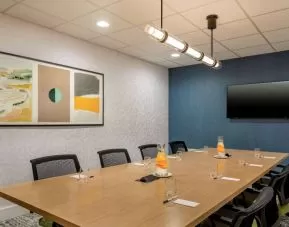 Meeting room in Sonesta Select Boston Foxborough Mansfield with long wooden table, eight chairs, and a large, wall-mounted TV.