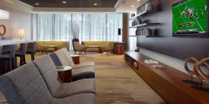Sonesta Select Atlanta Cumberland Galleria’s lobby has a large, wall-mounted TV, comfortable seating, and coffee tables.