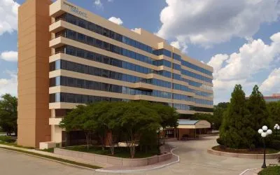 Sonesta Select Atlanta Cumberland Galleria’s exterior has the name on the building, numerous trees, and a covered entranceway.