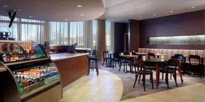Sonesta Select Atlanta Cumberland Galleria’s dining area features a bar, both tall stool and table seating, and large windows.