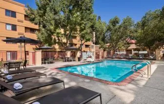 The outdoor pool at Sonesta Select San Jose Airport features a lift, and has nearby sun loungers and shaded tables and chairs.