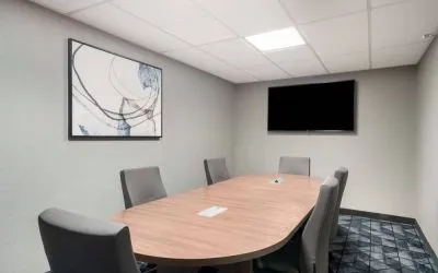 Hotel meeting room, with half a dozen chairs set around a wooden table, and a large TV on the wall.