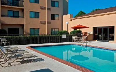 Sonesta Select Charlotte University Research Park’s outdoor pool has sun loungers and a shaded table and chairs by the side.