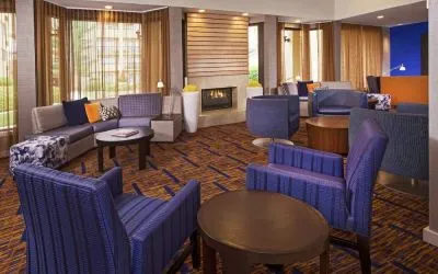 Sonesta Select Charlotte University Research Park’s lobby is furnished with a fireplace, large windows, coffee tables, and comfortable seating.