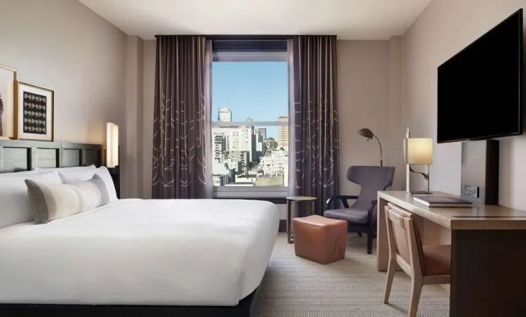 Double bed guest room in The Clift Royal Sonesta, with window, workspace desk/chair, and a large TV.