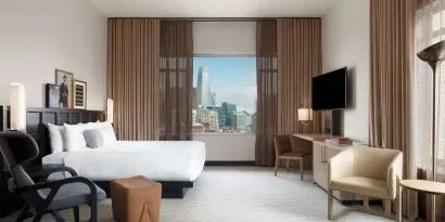 Double bed guest room in The Clift Royal Sonesta, featuring numerous chairs, a desk, coffee table, TV, and window with city views.