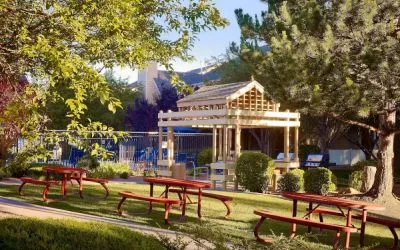The picnic area at Sonesta ES Suites Flagstaff features benches on tables on grass, with trees and and barbecue facilities nearby.