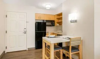 Sonesta ES Suites Charlotte Arrowood guest room kitchen area, with fridge-freezer, small table, sink, oven, and microwave.