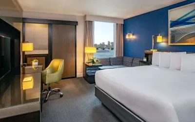Double bed guest room in Royal Sonesta Boston, furnished with corner sofa and coffee table, comfy chair, and wall-mounted TV.