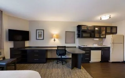 Sonesta Simply Suites Des Moines guest room, furnished with bed, kitchenette, TV, and workspace desk and chair.
