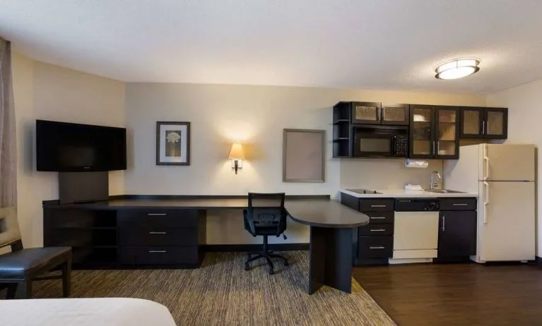 Sonesta Simply Suites Des Moines guest room, furnished with bed, kitchenette, TV, and workspace desk and chair.