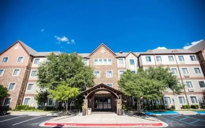 The hotel’s exterior has a covered entranceway flanked by trees, in addition to numerous parking spaces.