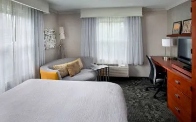 Double bed guest room in Sonesta Select Tinton Falls Eatontown, including workspace desk and chair, sofa, TV, and windows.