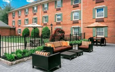 Sonesta Select Tinton Falls Eatontown’s patio is furnished with shaded tables and chairs, in addition to sofa and armchair seating, with greenery nearby.