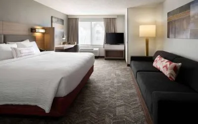Sonesta Select Seattle Renton double bed guest room, with sofa, workspace desk and chair, TV, and large window.