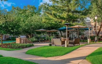 Sonesta ES Suites Parsippany Morris Plains’ barbecue area is furnished with tables and chairs, plus armchair seating, amid numerous trees.