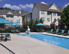 The outdoor pool of Sonesta ES Suites Birmingham Homewood is equipped with a lift, and both sun loungers and shaded tables/chairs are in the vicinity.