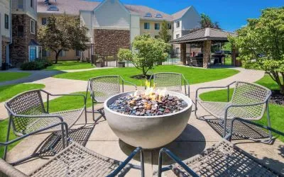 Sonesta ES Suites Andover Boston’s fire-pit is located amid pleasant greenery and surrounded by chairs, with the gazebo and barbecue facilities nearby.