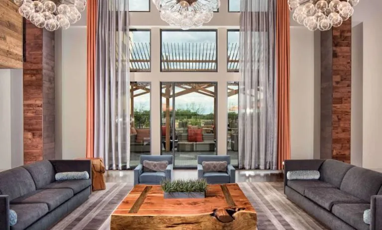 Sonesta Bee Cave Austin’s lobby lounge is furnished with armchair and sofa seating amid an airy setting, with the patio just steps away.
