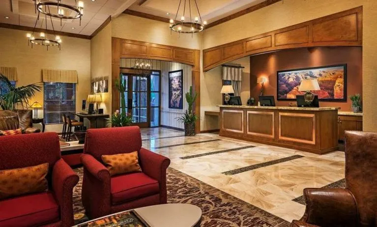 Sonesta Suites Scottsdale Gainey Ranch’s lobby has many potted plants, including cacti, a marble floor, and comfortable armchairs around a coffee table.