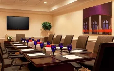 Meeting room in Sonesta Atlanta Airport North, furnished with long wooden table, a dozen chairs, and art and a widescreen television on the walls.