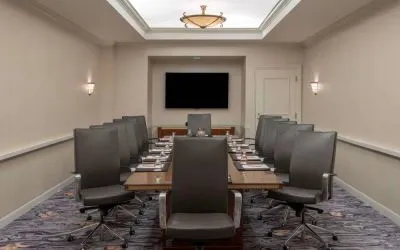 Sonesta Charlotte Executive Park meeting room, furnished with long table, a dozen leather swivel chairs, and a large, wall-mounted TV.