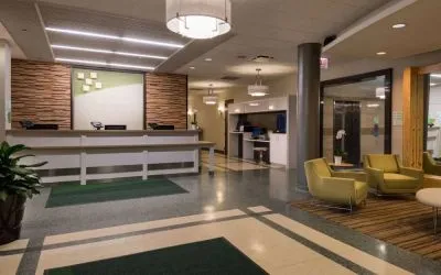The hotel lobby has yellow armchairs, potted plants, and a business center workstation, in addition to the reception desk.