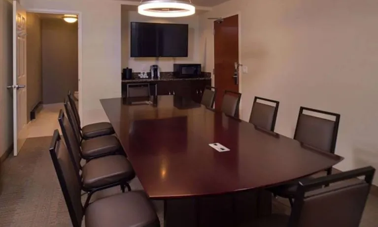 Meeting room in Sonesta Chicago O'Hare Airport Rosemont, featuring long wooden table, 10 chairs, a microwave, and a large TV.