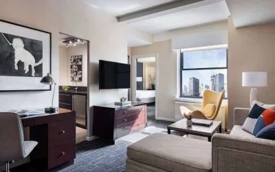 The Shelburne Sonesta New York guest room living area, including sofa, chairs, coffee table, and TV.
