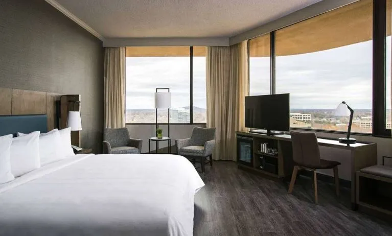 Double bed guest room in Sonesta Nashville Airport, furnished with chairs, coffee table, TV, large windows, and a workspace desk and chair.