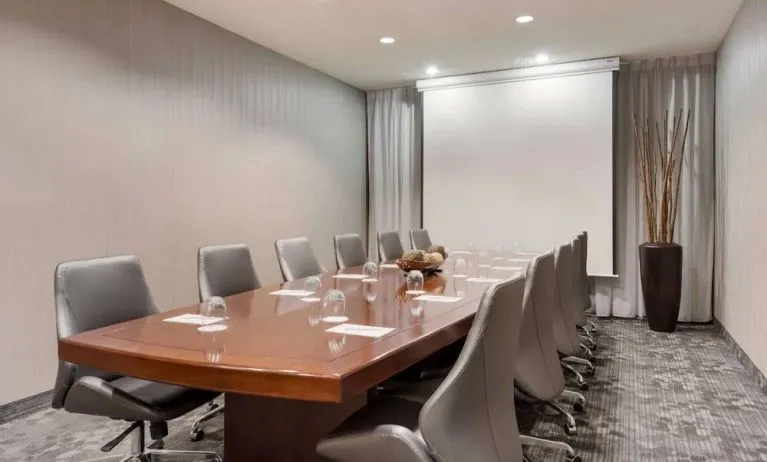 Sonesta Select Tempe Downtown meeting room, featuring long wooden table, a dozen swivel chairs, and a projector screen.