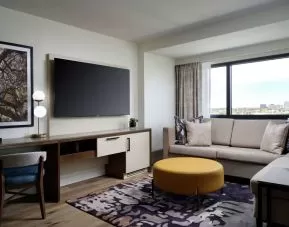 Sonesta Irvine guest room living area, including corner sofa, chair, window, and large, wall-mounted TV.