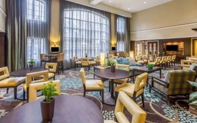 The hotel’s breakfast area has a carpeted floor, range of table sizes, seating from normal chairs to tall stools and armchairs, high ceilings and large windows, plus multiple TVs.