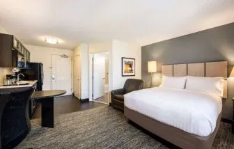 Double bed guest room in Sonesta Simply Suites Atlanta Gwinnett Place, including kitchen, table, and an armchair.
