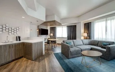 Guest room living area in Sonesta Columbus Downtown, including corner sofa and coffee table, large windows, and a TV with table and chairs nearby.