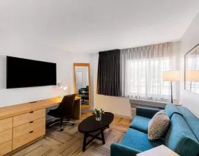 Sonesta Simply Suites Austin South guest room living area, furnished with sofa, coffee table, chair, and wall-mounted TV.